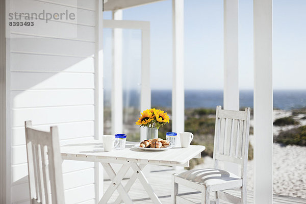 Vase mit Blumen  Kaffee und Gebäck auf Terrassentisch mit Blick aufs Meer