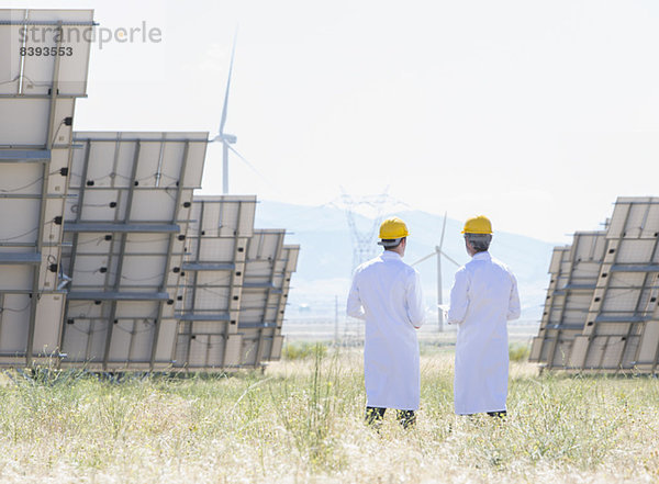 Wissenschaftler stehen bei Sonnenkollektoren in ländlicher Landschaft