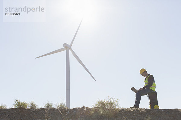 Arbeiter mit Laptop per Windkraftanlage in ländlicher Landschaft