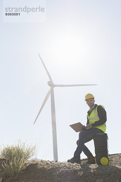 Arbeiter mit Laptop per Windkraftanlage in ländlicher Landschaft