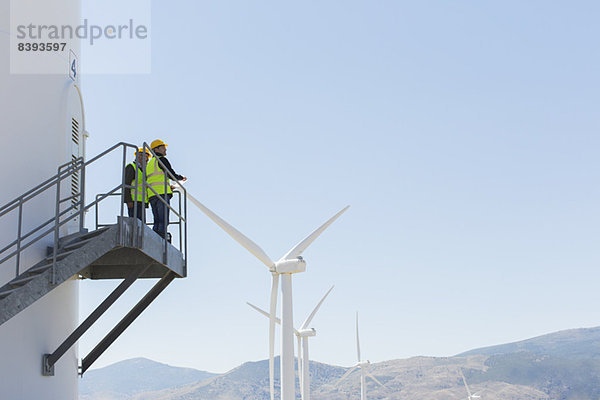 Arbeiter  die auf einer Windkraftanlage in ländlicher Landschaft stehen