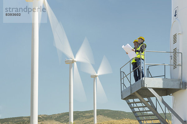 Arbeiter  die auf einer Windkraftanlage in ländlicher Landschaft stehen