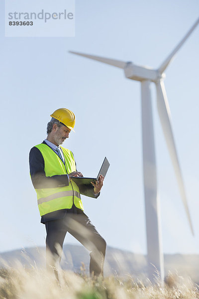 Arbeiter mit Laptop per Windkraftanlage in ländlicher Landschaft