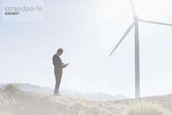 Geschäftsmann mit Laptop per Windkraftanlage in ländlicher Landschaft