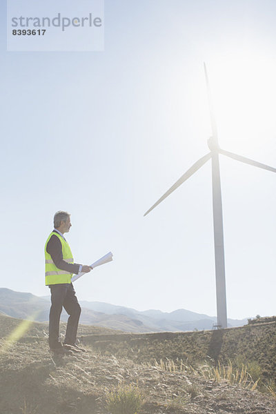 Geschäftsmann untersucht Windkraftanlage in ländlicher Landschaft