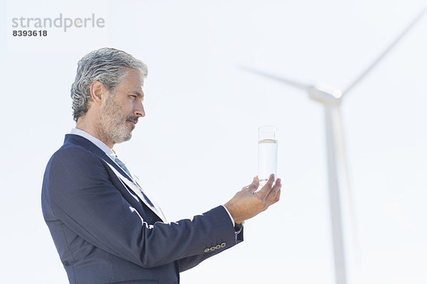 Geschäftsmann untersucht Wasserglas mit Windkraftanlage