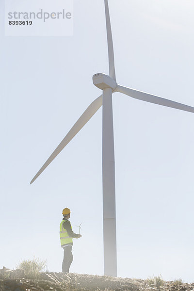 Geschäftsmann untersucht Windkraftanlage in ländlicher Landschaft