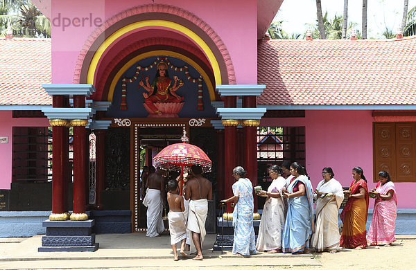 Eine Gruppe von Frauen mit Opfergaben und ein Priester umrunden einen Hindu-Tempel  Varkala  Kerala  Indien