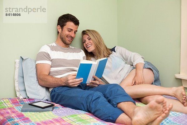 Paar entspannt auf dem Bett mit Blick auf das Buch