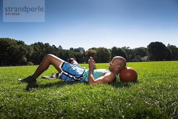 Junger Mann auf Gras liegend mit Kopf auf Basketball