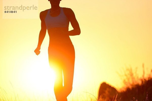 Silhouette einer jungen Frau  die bei Sonnenuntergang läuft.