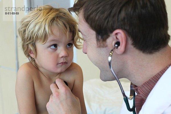 Junge männliche Ärztin hört auf die Brust der Jungen in der Klinik