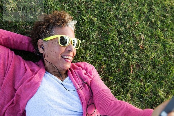 Porträt einer älteren Frau auf Gras liegend mit Sonnenbrille