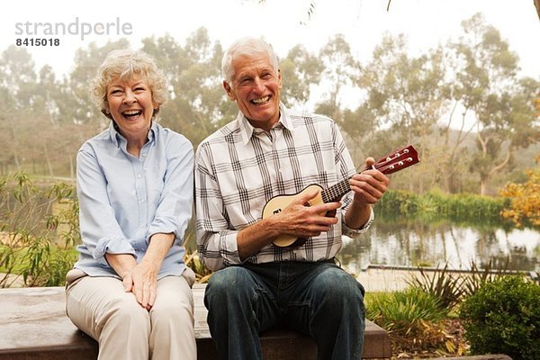 Ehemann spielt Ukulelele mit Frau am See