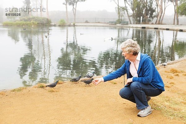 Seniorin beim Füttern von Tauben am See