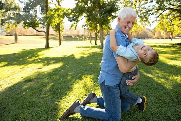 Großvater kniend auf Gras umarmendem Enkel