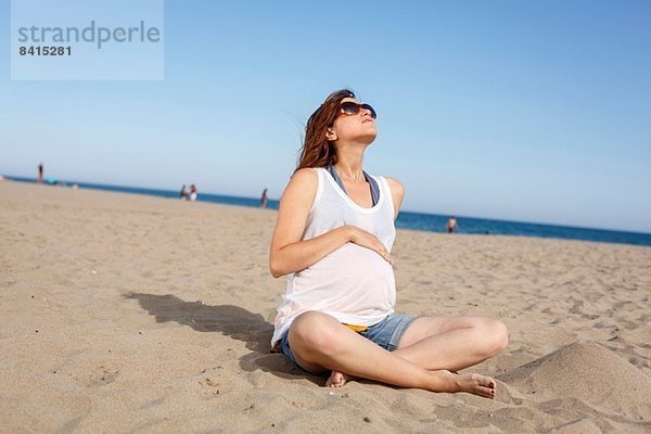 Schwangere Frau am Strand sitzend
