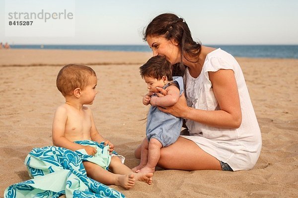 Mutter und Babys am Strand sitzend