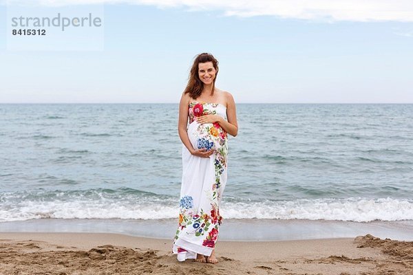 Schwangere Frau am Strand stehend  Hände auf dem Bauch