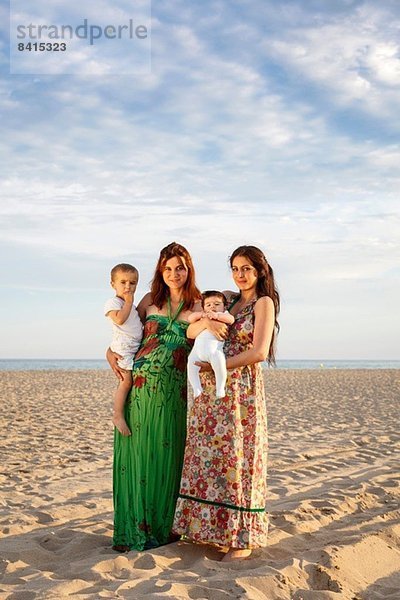 Mütter stehen am Strand und halten Baby und Kleinkind.