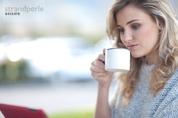 Junge Frau sitzt vor dem Café mit Tasse Kaffee und digitalem Tablett