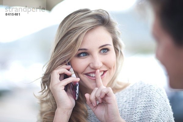 Junge Frau am Telefon mit Finger auf den Lippen