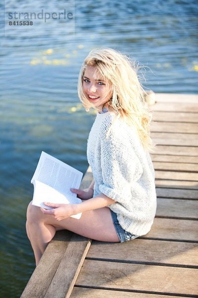 Junge Frau auf dem Pier sitzend  Buch haltend