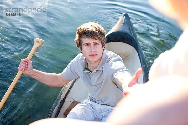 Junger Mann im Ruderboot  der bis zu weiblichen Freunden reicht.
