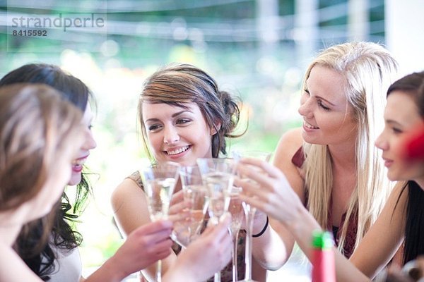 Junge Frau und Freunde stoßen mit einem Glas Champagner an.