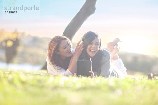 Zwei junge Frauen im Park mit digitalem Tablett und Kopfhörer