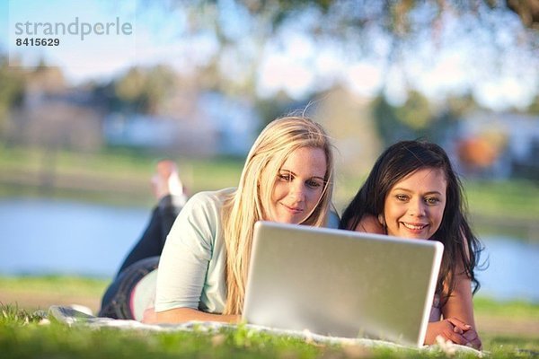 Zwei junge Frauen im Park mit Blick auf den Laptop