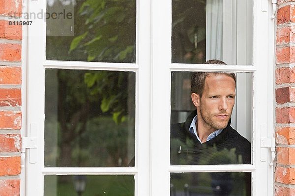 Mittlerer Erwachsener Mann  der aus dem Fenster schaut.