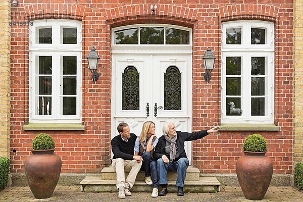 Vater und mittleres erwachsenes Paar auf der Türschwelle sitzend