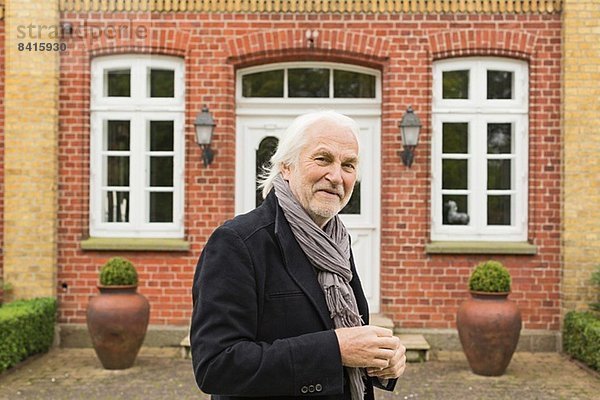 Porträt eines älteren Mannes mit Jacke und Schal vor dem Haus