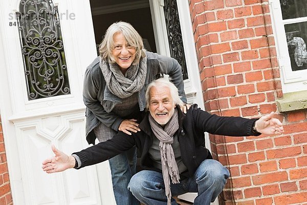 Älteres Ehepaar vor der Haustür  Mann kauert mit offenen Armen