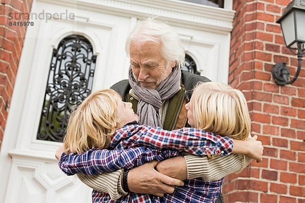 Großvater umarmt Enkelkinder vor der Haustür