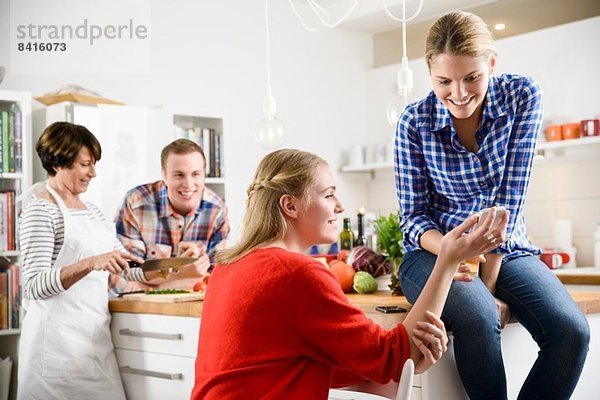Zwei Frauen mit Handy in der Küche  Mutter und Bruder im Hintergrund