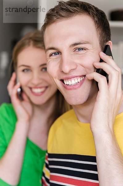 Junger Mann am Handy mit Frau im Hintergrund