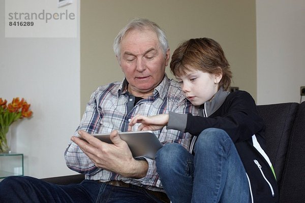 Senior Mann mit Enkel zu Hause mit digitalem Tablett