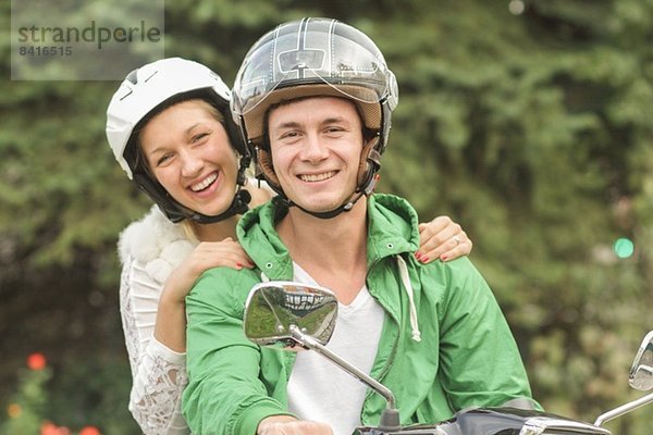 Porträt eines jungen Paares in Helmen auf Vespa sitzend