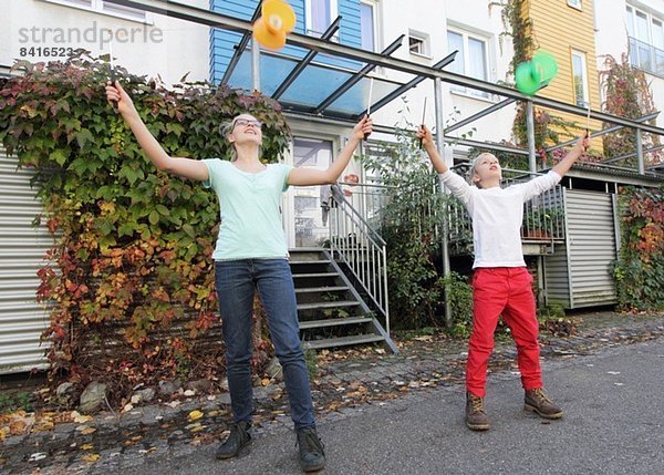 Geschwister spielen mit Kreiseln vor dem Haus