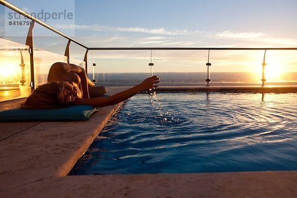 Frau bei Sonnenuntergang am Schwimmbad liegend