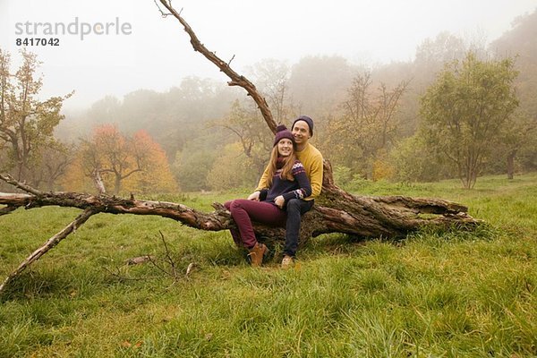 Junges Paar sitzend auf nacktem Baum im nebligen Park