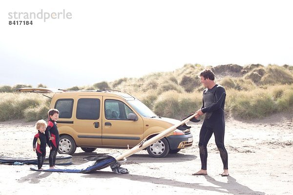 Vater mit zwei Söhnen  Surfbrett und Auto am Strand