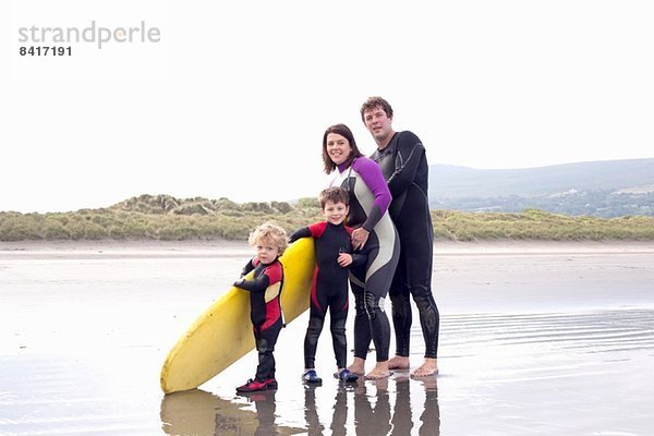 Familie mit zwei Jungen und Surfbrett am Strand