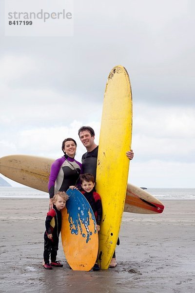 Familienporträt mit zwei Jungen mit Surfbrettern am Strand