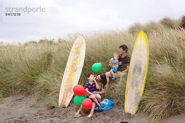 Familie mit zwei Jungen am Strand mit Surfbrettern