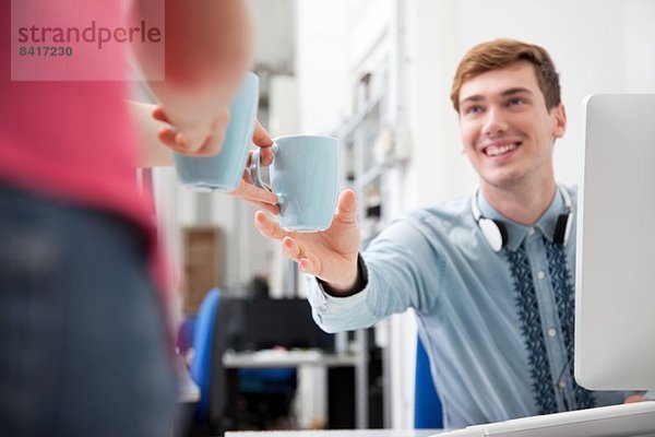 Frau gibt jungen Mann Kaffee im Büro