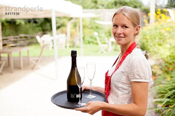 Portrait der Kellnerin mit Weinschale und Gläsern im Cafégarten