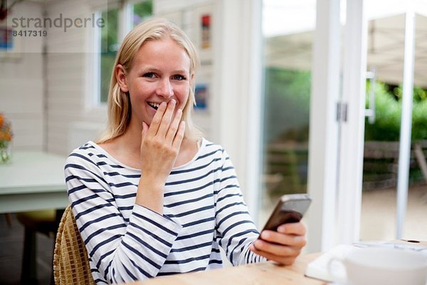 Junge Frau im Cafe lacht über Handy